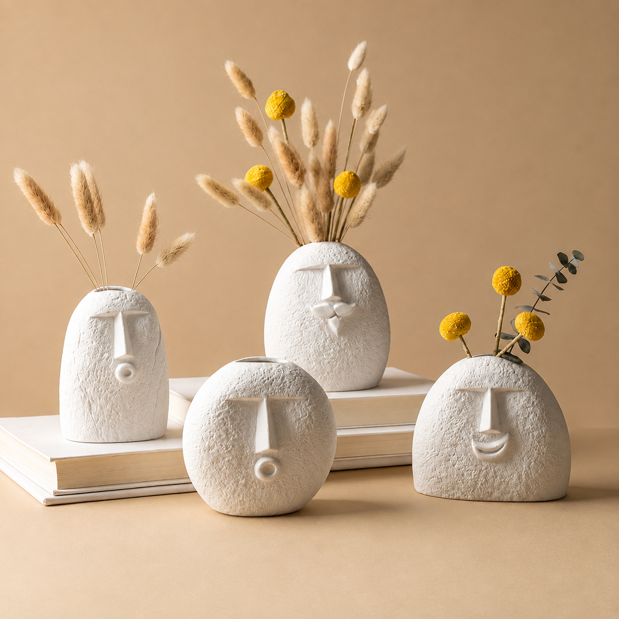 Four abstract face ceramic vases with dried botanicals on a warm beige surface