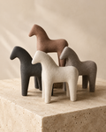 Set of four ceramic horse sculptures in cream, brown, black and grey on a travertine surface