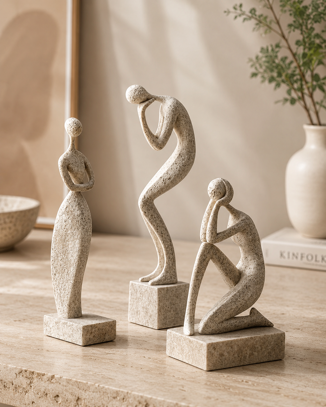 Set of three abstract ceramic figure sculptures on a travertine console with greenery