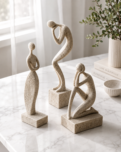 Three abstract figure sculptures on a white marble surface with soft natural light
