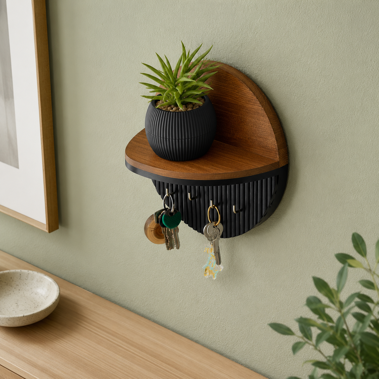 Circular wood and black key holder with 4 gold hooks styled on a sage green wall with plant
