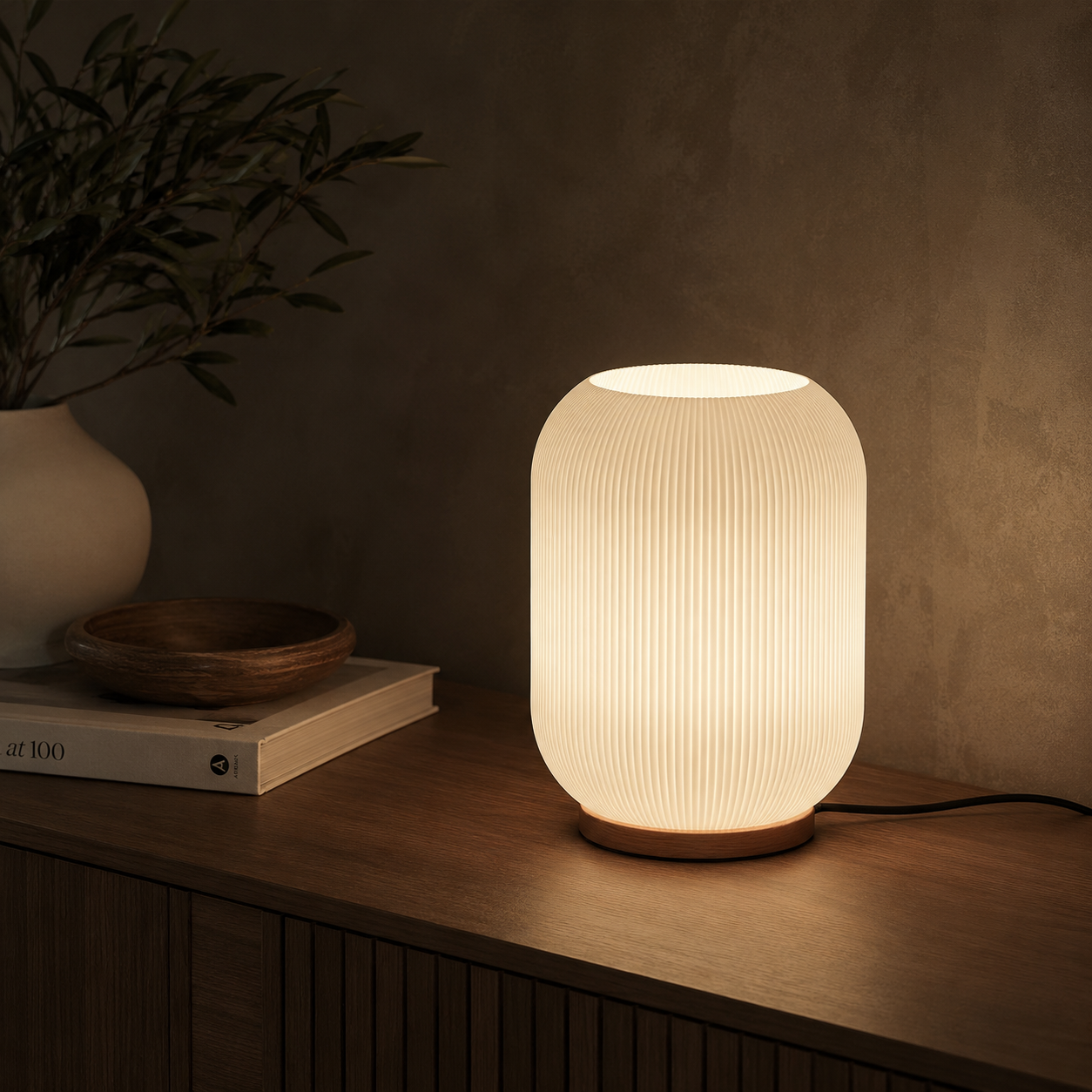 Ribbed glass table lamp glowing on a dark wood console with wooden bowl and olive branch