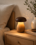 Mushroom wood table lamp glowing warm amber on an oak bedside table with books and ceramic vase