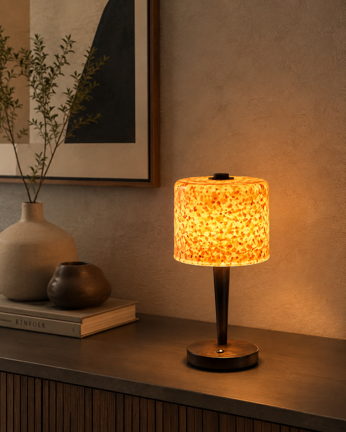 Amber tortoiseshell glass lamp on a dark ribbed sideboard with ceramic vases and books in a moody living room