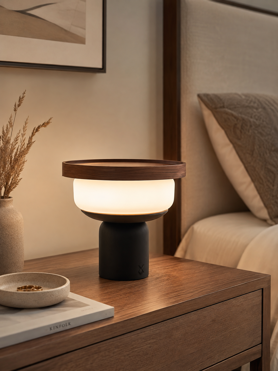 Walnut tray table lamp with opal glass globe glowing on a dark wood bedside table with dried pampas grass and ceramic dish