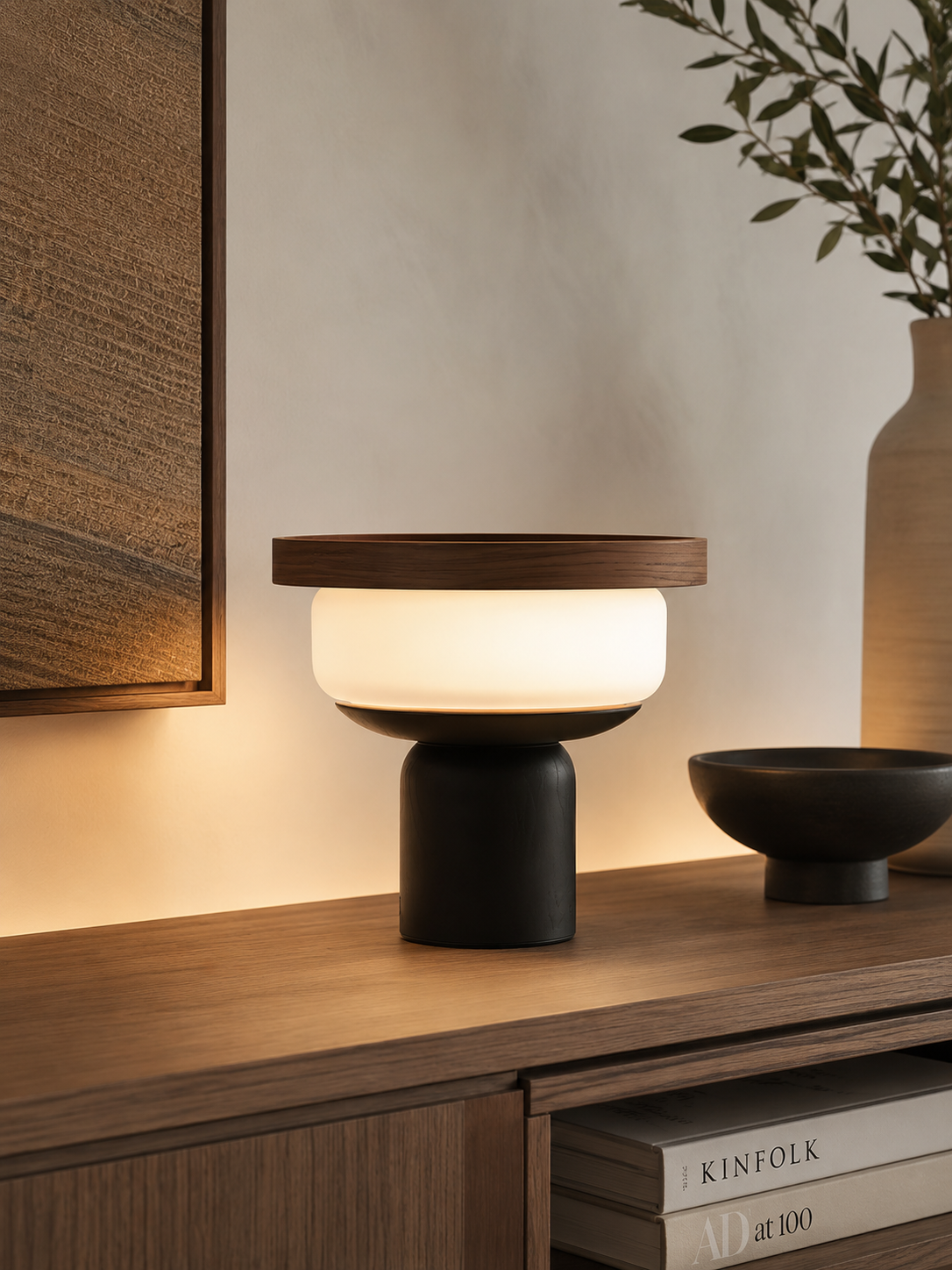 Walnut tray table lamp glowing on a dark wood console with olive branch, ceramic bowl and art books