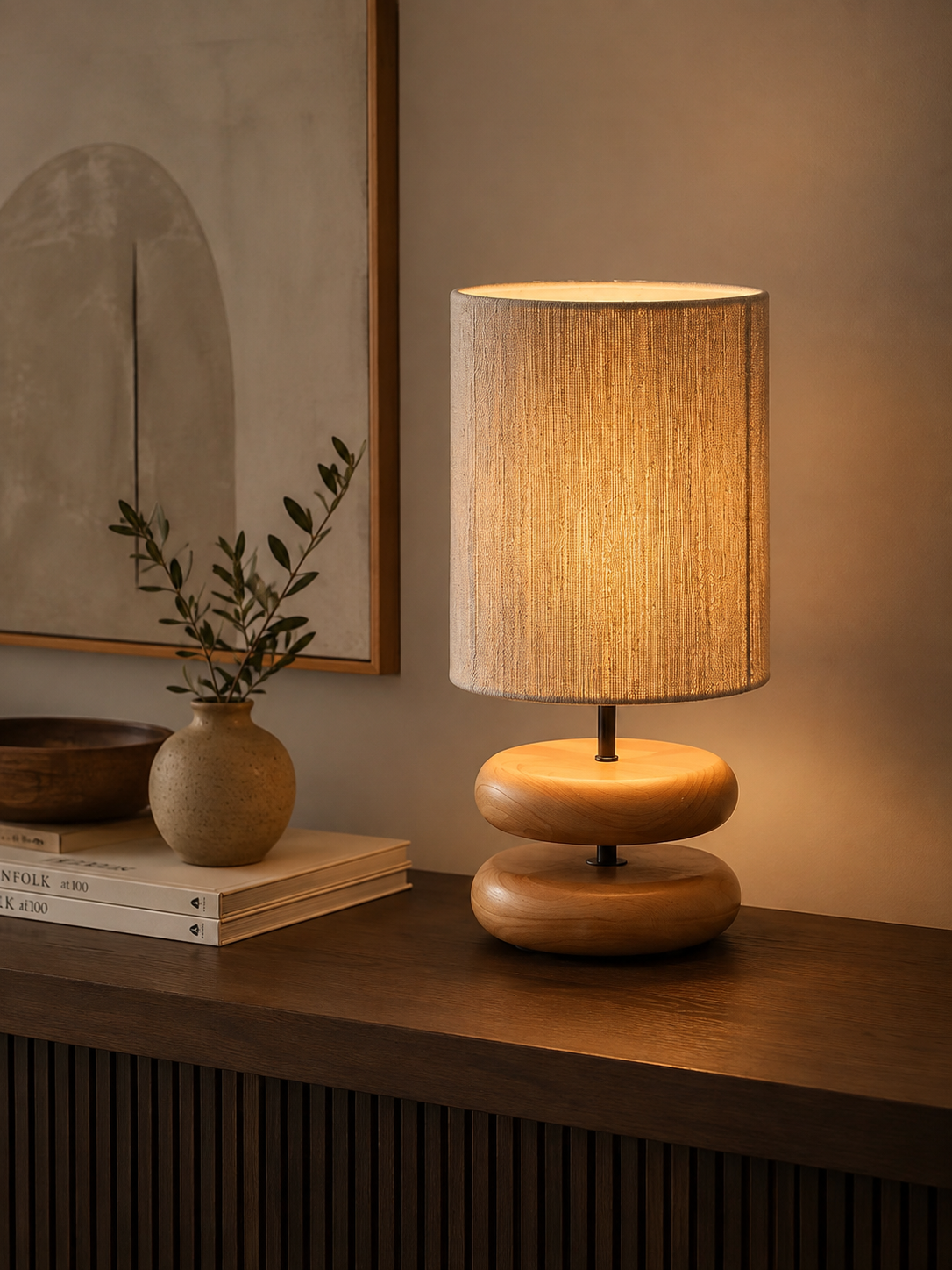 Stacked pebble wood lamp on a dark ribbed sideboard with Kinfolk books, ceramic vase and olive branch