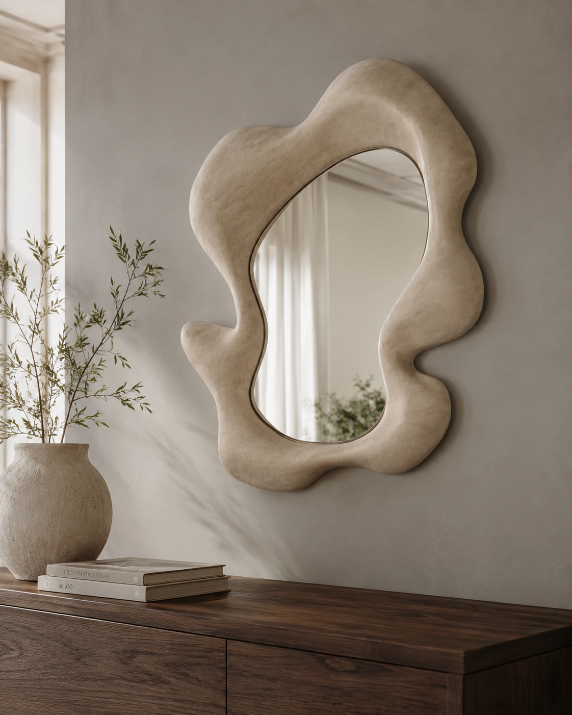 Sculptural wave mirror with cream plaster frame on a grey wall above a dark wood console with ceramic vase
