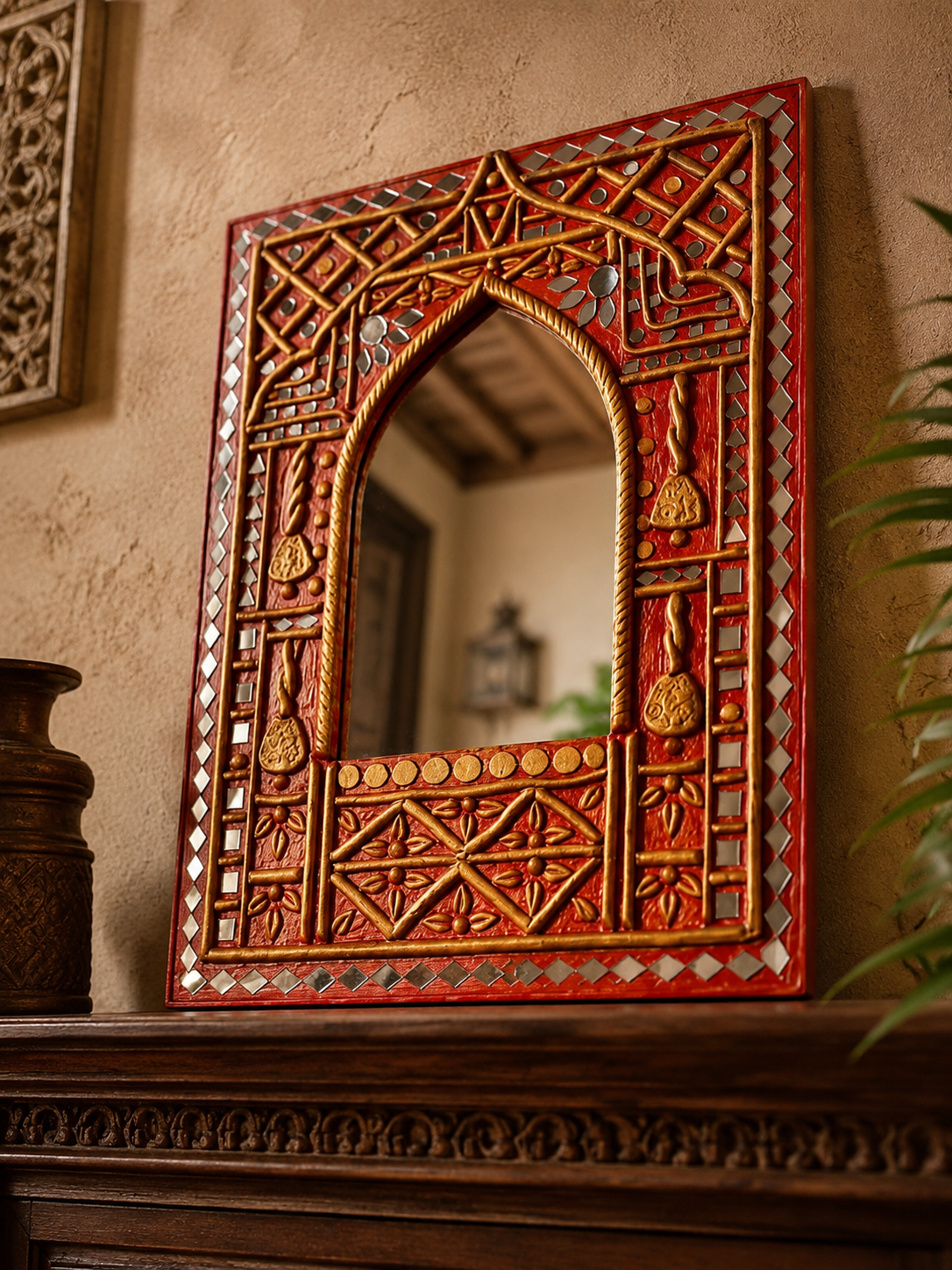 Hand-carved Rajasthani mirror with gold lattice and mirror tile inlay displayed on a dark carved wood mantle with brass vase