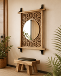 Hand-carved mango wood jali mirror with shelf and black iron brackets in a warm entryway with wooden stool and plants