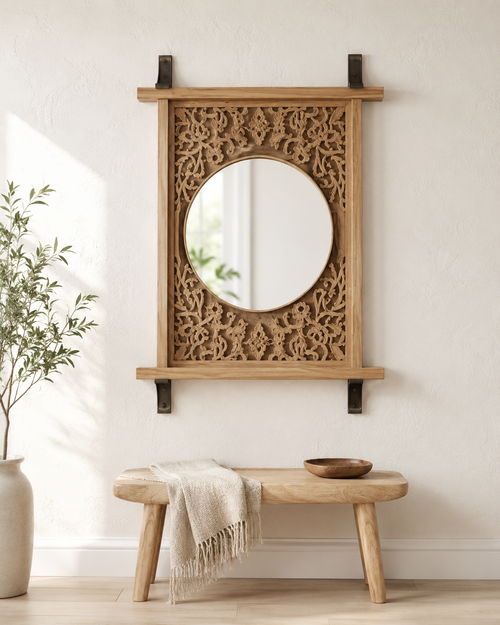 Carved wood jali mirror with round mirror and display shelf on a white wall above a wooden bench with linen throw and wooden bowl